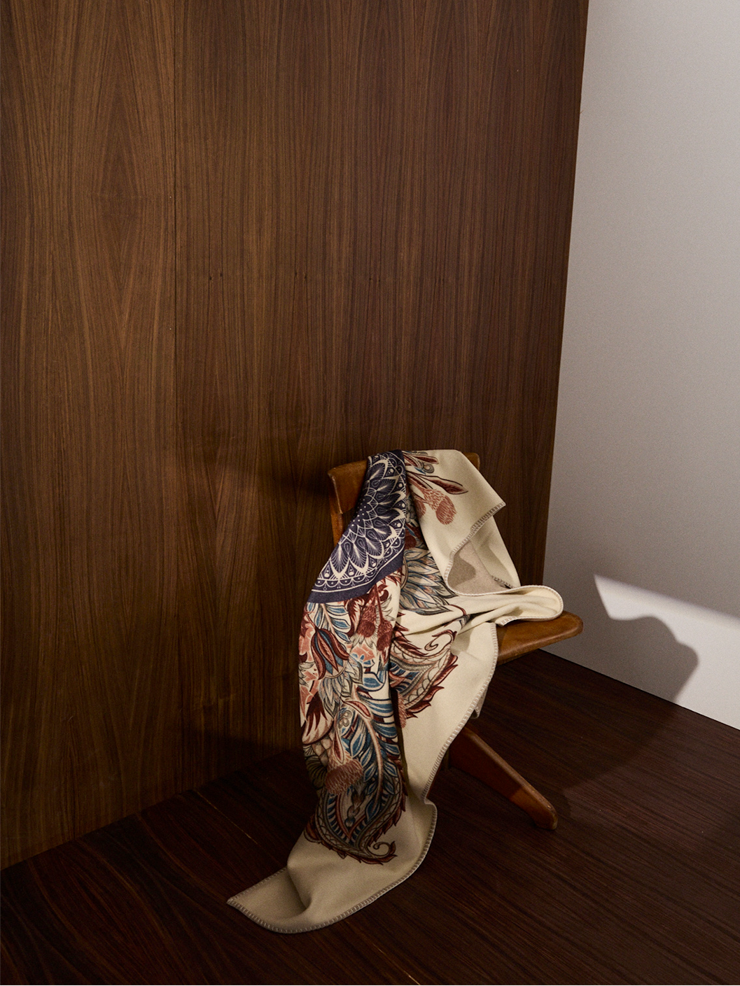 Decorative scarf draped over a wooden chair against a wooden wall.